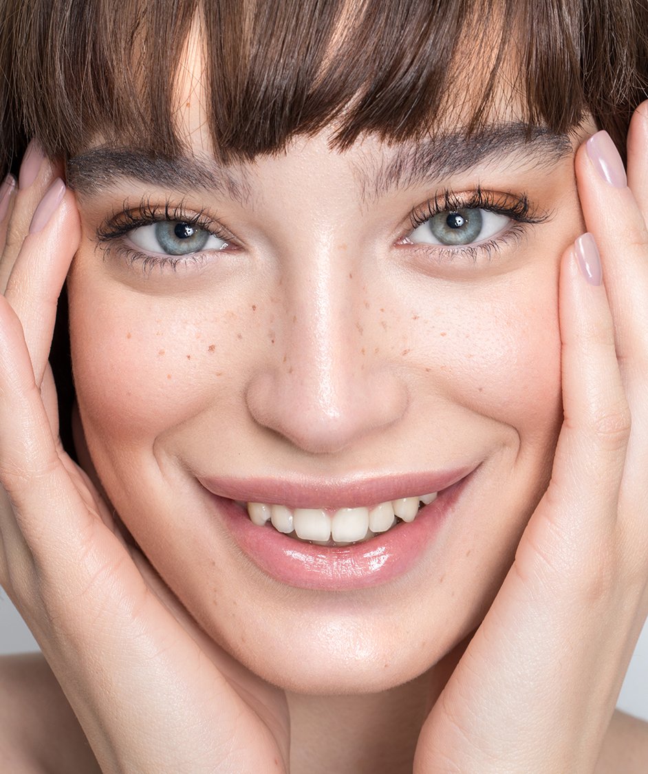 smiling woman with brown hair and blue eyes holding her hands to her face