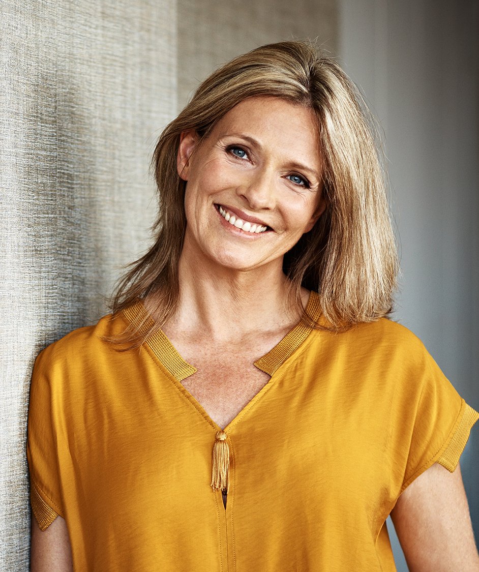 smiling woman in yellow shirt leaning against wall with long hair