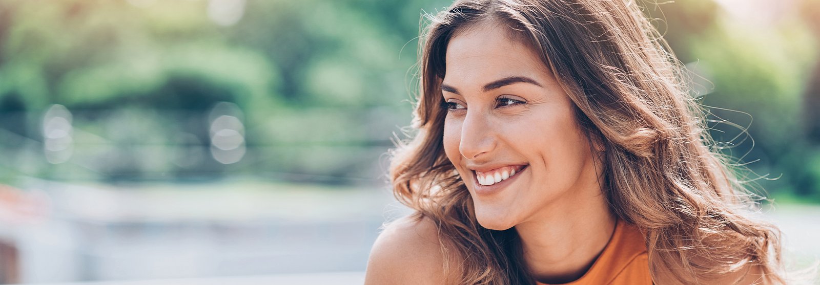 smiling woman with long brown hair and orange top looking at camera