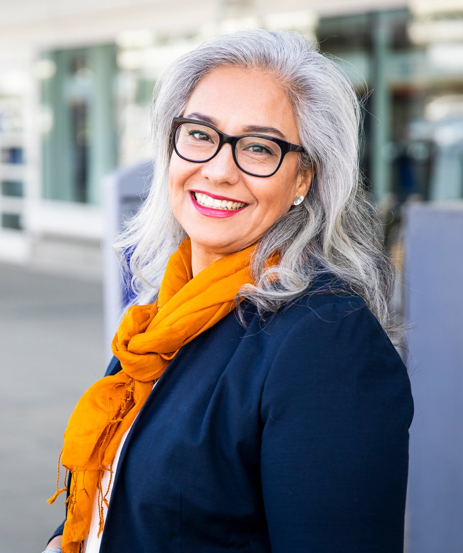 Beautiful older woman with grey hair smiling, wearing a blue coat and yellow scarf